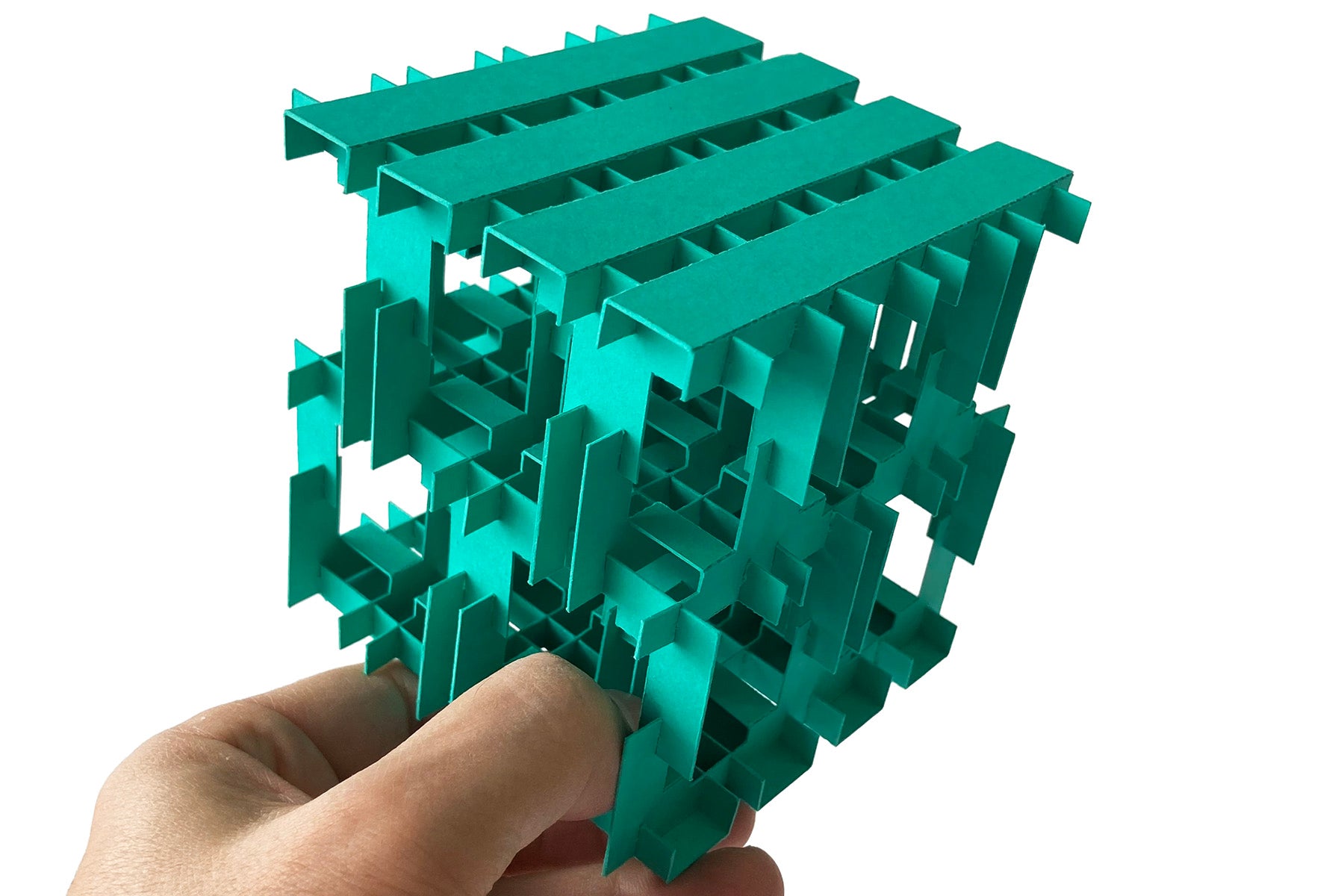 Green geometric folded paper puzzle cube held by a hand on a white background