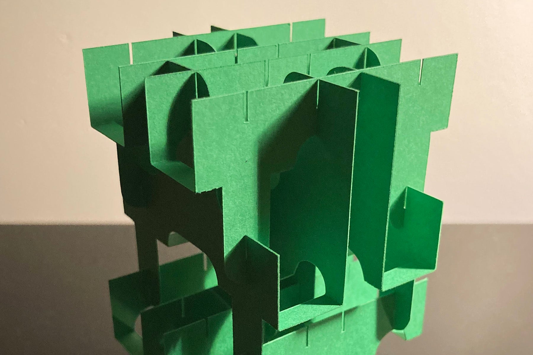 Green geometric sculpture on a reflective surface with a neutral background