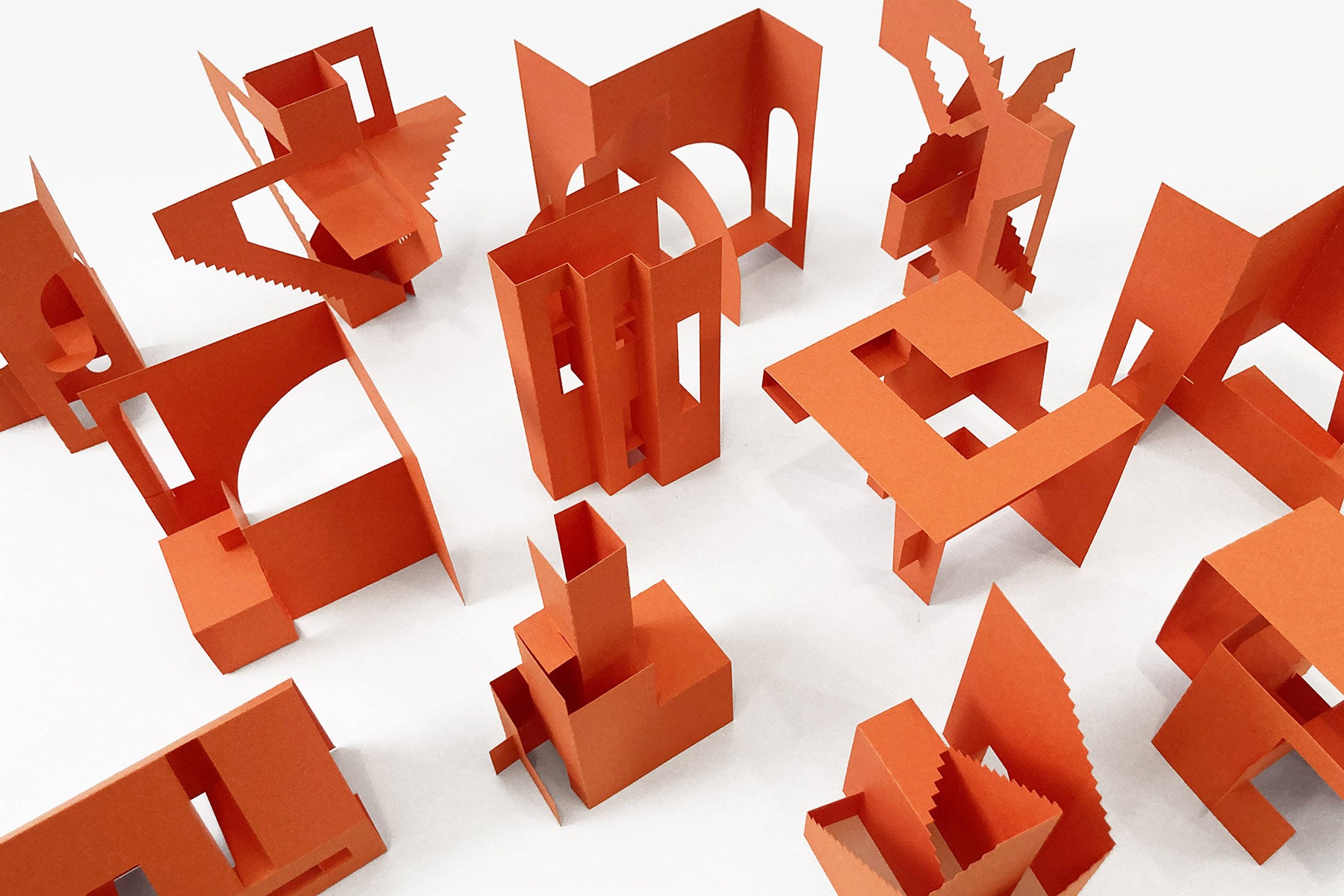 Orange architectural paper models scattered on a white background