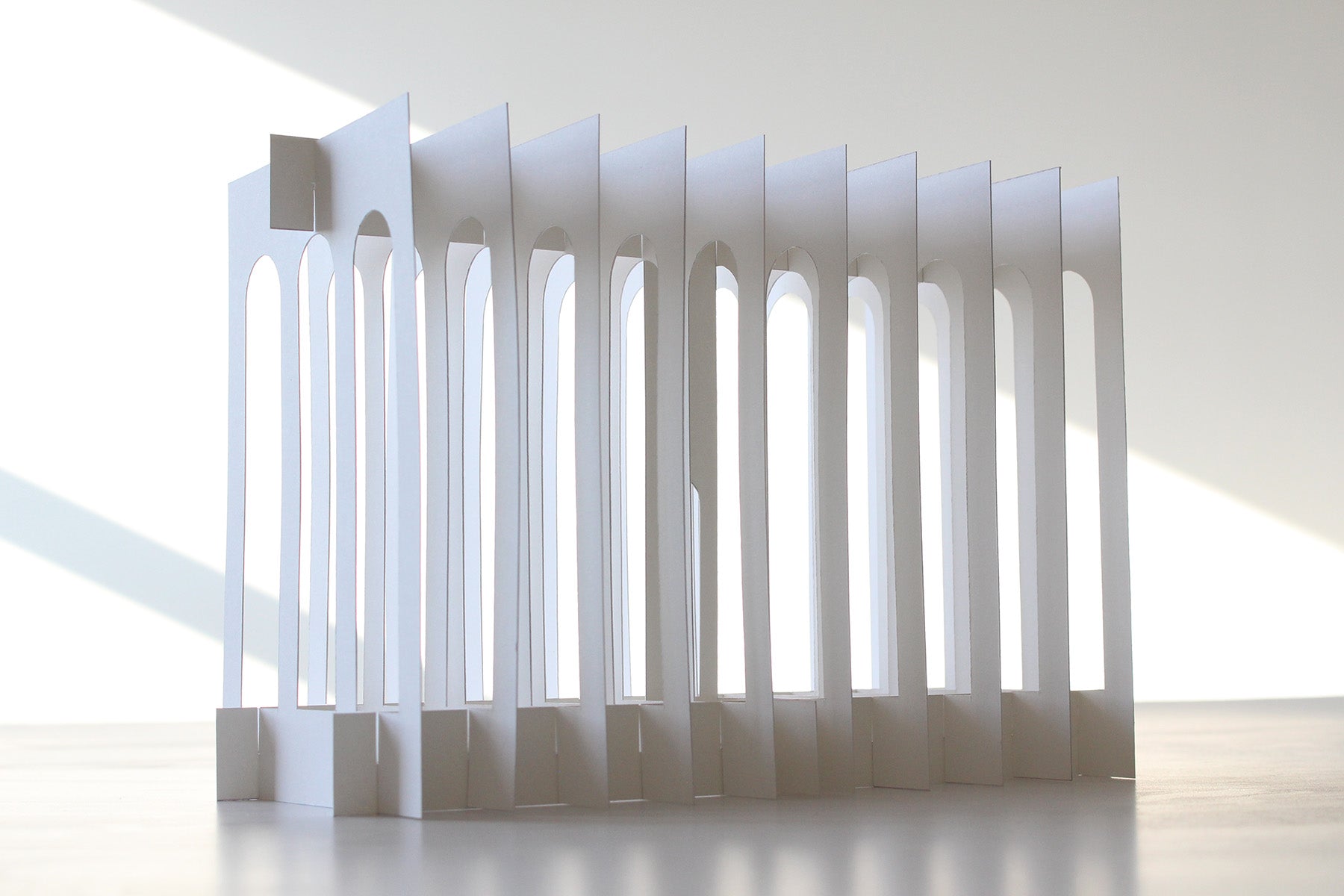 Modern architectural paper design with vertical white arches in a minimalistic setting