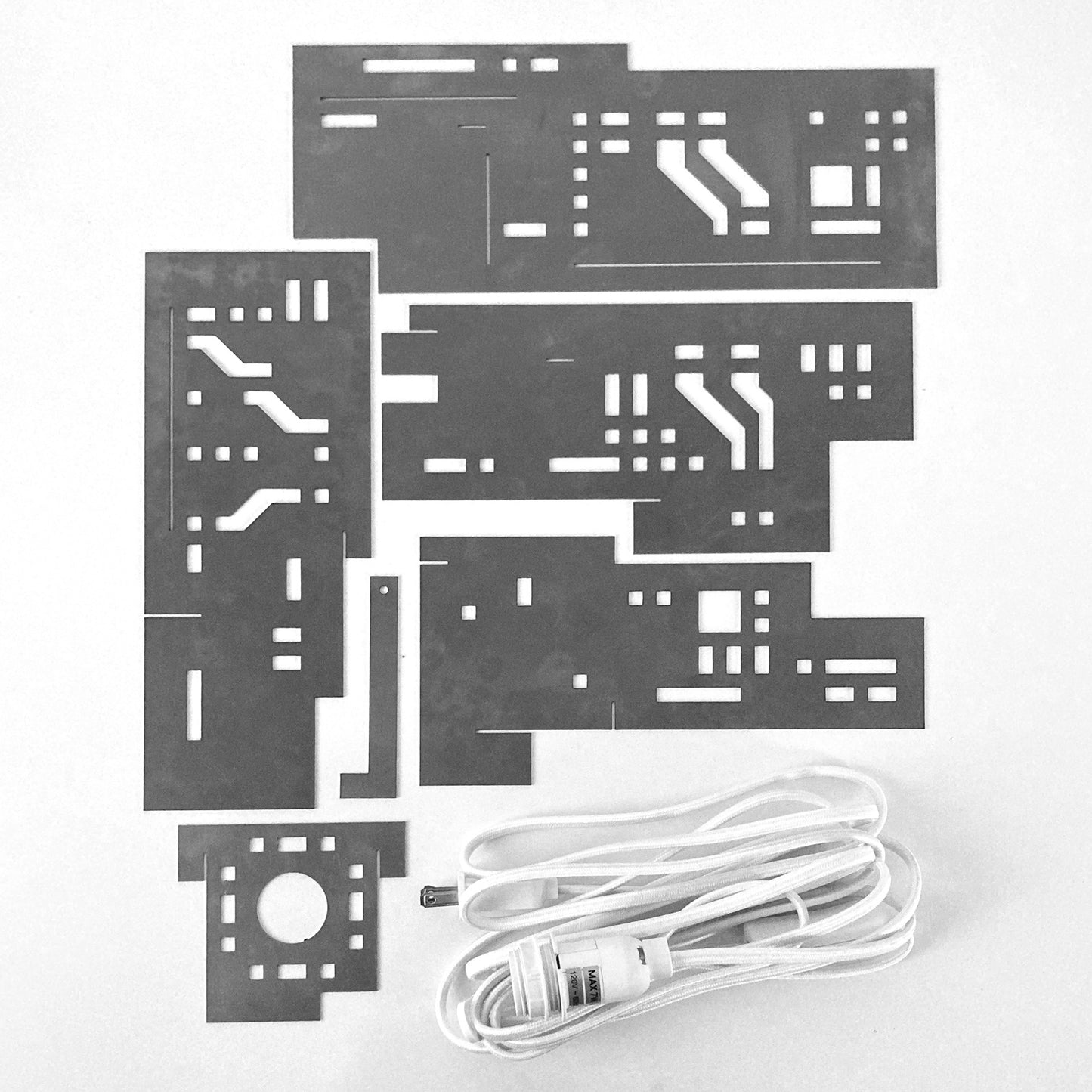 Flat layout of steel sheet metal parts and light socket cord used to assemble an architectural cityscape table lamp.