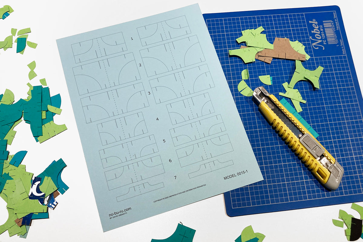 Cutting mat with grid lines, cardstock pieces, and a cutter on a white background