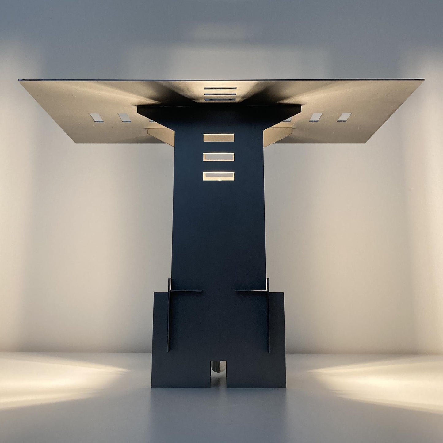 Illuminated modern cold rolled steel sculptural lamp casting shadows on a white background