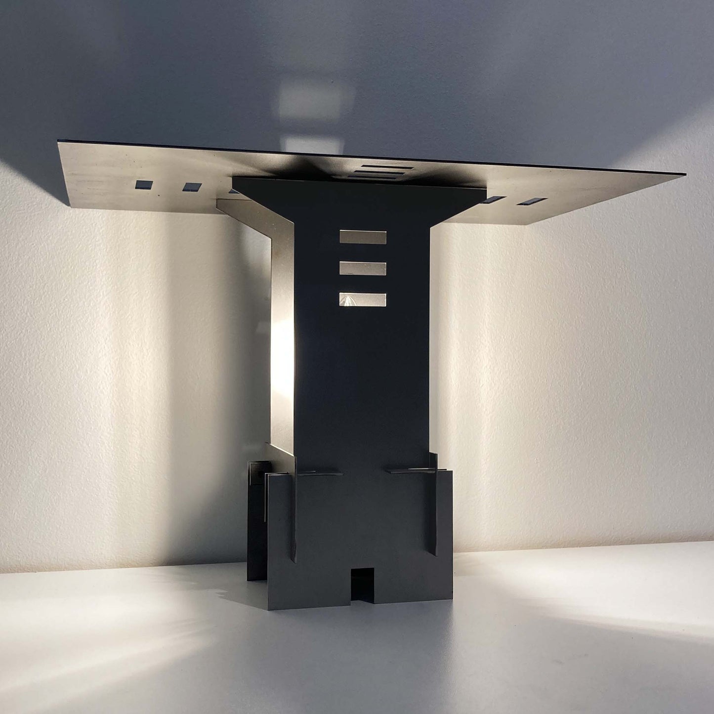 Illuminated modern cold rolled steel sculptural lamp casting shadows on a white background